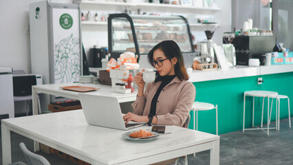 Asian businesswoman working on a laptop while drinking a cup of coffee in a cafe
