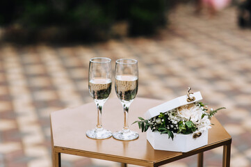 Glass wine glasses with champagne, a box of flowers are on the table at the wedding ceremony. Close-up photo.