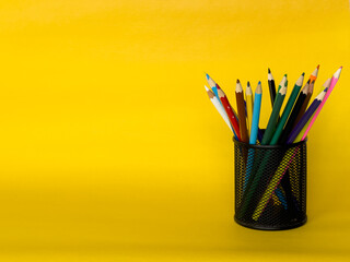 cylinder shaped metal net box pencil holder isolated on yellow background. many colored pen ,...