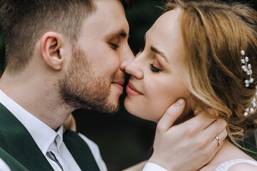 A stylish bearded groom and a beautiful blonde bride gently hug, kiss close-up. Wedding photography, portrait of happy smiling newlyweds.