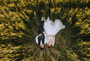 A stylish groom and a beautiful blonde bride in a white dress with a long veil in sunglasses lie in...