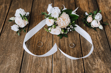 A bouquet of flowers with a ribbon in the form of a heart, a boutonniere, golden rings of the newlyweds lie on a wooden background. Wedding photography closeup, top view, concept.