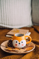 Autumn cozy home. Fall cozy reading nook with a blanket, candles, autumn fall leaves, cup of coffee on brown bed at home background. Cold season morning coffee, relaxing still life concept.