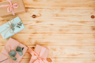 Background for greetings. Gifts wrapping in soft pink and blue paper with dry eucalyptus branches on a light wooden background. Top view