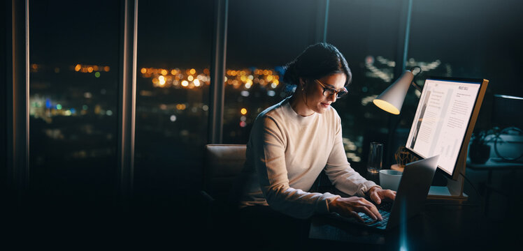 Working late in an office: Business woman using laptop at her desk