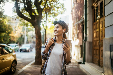 Happy young Asian woman using a smartphone while walking in the city