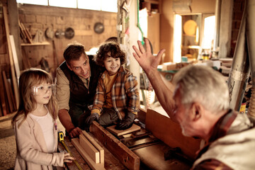 Grandfather carpenter teaching his son and grandchildren how to work with wood in a wood workshop