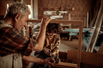 Grandfather carpenter teaching his grandson how to work with wood in a wood workshop