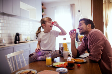Young single father having fun and eating breakfast with his daughter in the kitchen