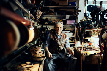 Portrait of a Senior and experienced male shoemaker or cobbler working and restoring a leather shoe in his old workshop
