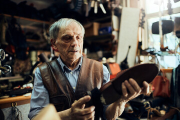 Obraz premium Senior male cobbler restoring a shoe in his old workshop in the city
