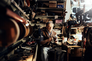 Obraz na płótnie Canvas Senior male shoemaker restoring a shoe in his old workshop in the city