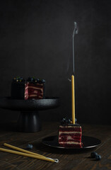 Selective focus candle with smoke in a piece of black birthday cake