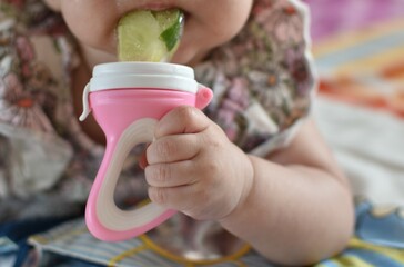 a small child holds in his hand a pacifier for fruits and vegetables with a cucumber inside