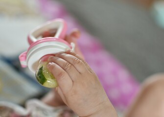 a small child holds in his hand a pacifier for fruits and vegetables with a cucumber inside