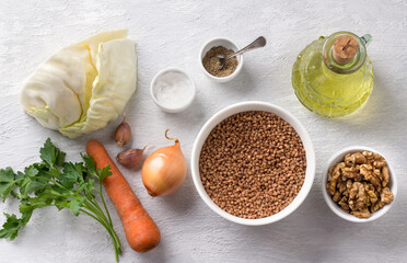 Ingredients for cooking vegan buckwheat with vegetables: buckwheat, cabbage, carrots, onions, garlic, walnuts, parsley, salt, pepper, vegetable oil on a light gray background
