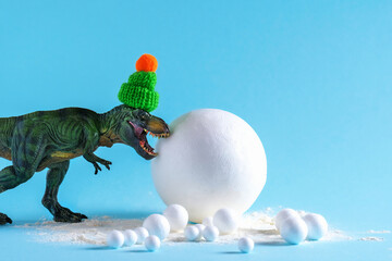 Cute green dinosaur with big snowball on blue background. Funny winter holidays card.