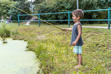 Naklejka premium little smiling child playing with a stick by a pond in a public park