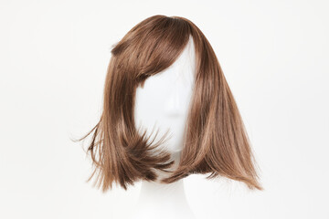 Natural looking dark brunet wig on white mannequin head. Middle length brown hair on the plastic wig holder isolated on white background, front view .