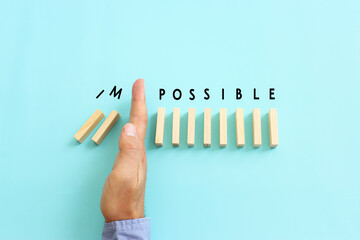 Male hand stopping the domino effect. Wooden cubes with the text impossible. Success and challenge concept