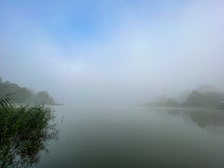 Mystical morning at the fog-kissed lake, where nature's beauty emerges through the ethereal mist.