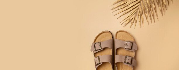 Trendy beige leather sandals, golden palm leaf on beige background, top view flat lay. Minimalistic...