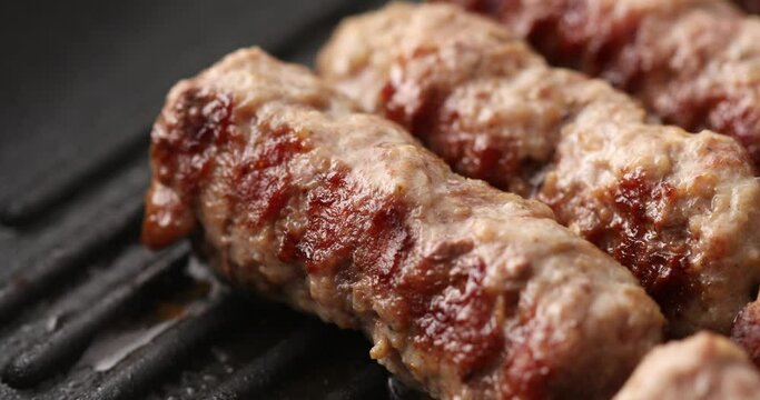Minced meat sausages are fryed on a grill pan with steam or smoke. Close-up dolly shot. Frying traditional Balkan chevapi. Cooking food.