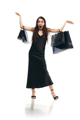 Black friday concept. Full length portrait of delighted women wearing black midi dress raising hands with bags because of start of sales.