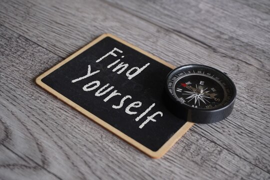 Closeup image of compass and chalkboard with text FIND YOURSELF on table.