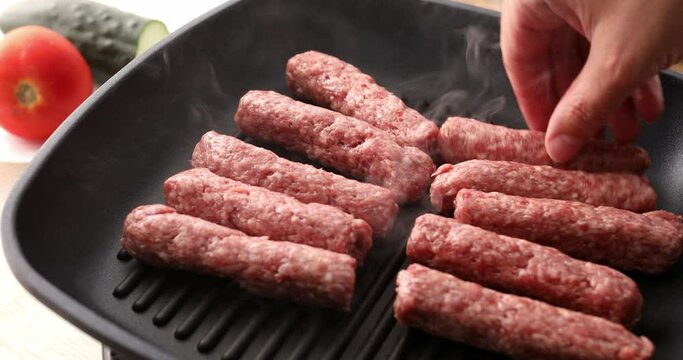 Raw minced meat sausages are placed on a grill pan. Frying traditional Balkan chevapi. Cooking food.
