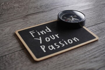Closeup image of compass and chalkboard with text FIND YOUR PASSION on table.
