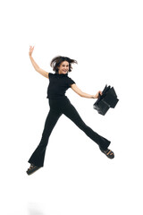 Portrait of jumping cheerful woman wearing fashion total black outfit holding bags in hands isolated on white studio color background. ad