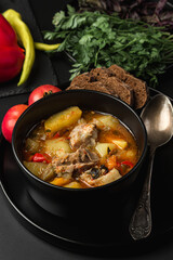 Stewed meat and vegetables in a black plate on a dark background