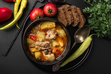 Stewed meat and vegetables in a black plate on a dark background
