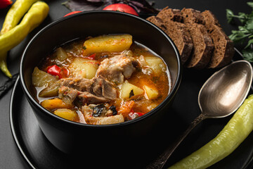 Stewed meat and vegetables in a black plate on a dark background