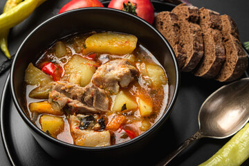 Stewed meat and vegetables in a black plate on a dark background