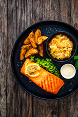 Grilled salmon steak with baked potatoes and sauerkraut served on wooden table 