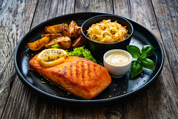 Grilled salmon steak with baked potatoes and sauerkraut served on wooden table 