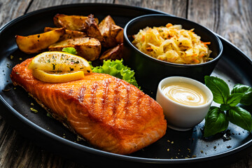 Grilled salmon steak with baked potatoes and sauerkraut served on wooden table 