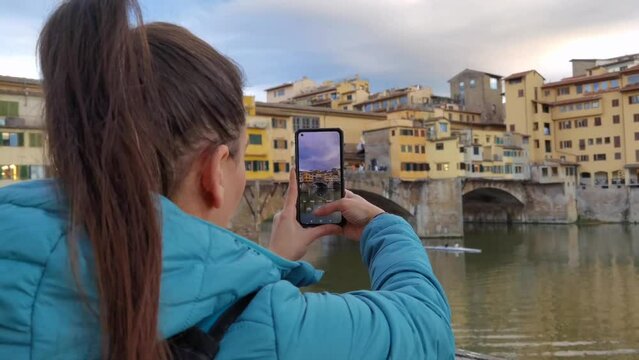 A tourist visiting Florence taking a picture of the famous Ponte Vecchio