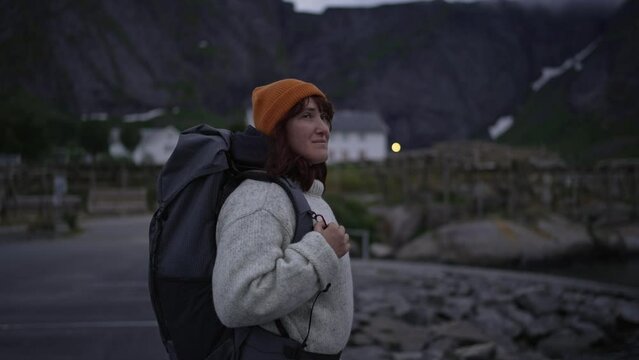 With a backpack on her shoulders. female traveler is depicted up close as she immerses herself in the enchanting landscapes of Lofoten Island, Northern Norway, during the nighttime hours.