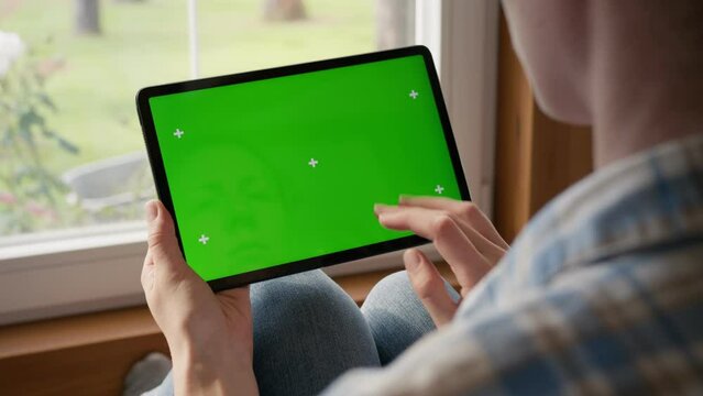 tablet computer with green screen chromakey display with motion trackers in woman hand at home, with window on background. finger scroll and tap gesture.