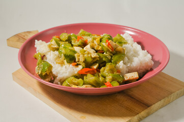 A plate of white rice with stir-fried oyong or luffa gourd and sliced yellow tofus on a wooden board isolated on a white background