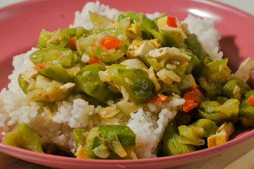 a plate of white rice with stir-fried oyong or luffa gourd and sliced yellow tofus on a wooden board isolated on a white background