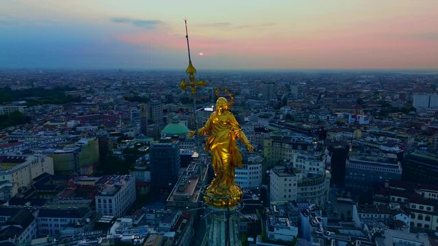 Aerial view of the Madonna statue on the central spire of the duomo and goroda cathedral at sunrise. Roofs of houses and skyscrapers. Sun over the horizon. duomo square. Milan. Italy, 10.2023