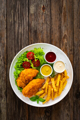 Seared breaded chicken nuggets with French fries and fresh vegetables on wooden table
