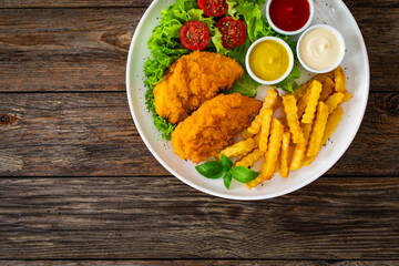 Seared breaded chicken nuggets with French fries and fresh vegetables on wooden table
