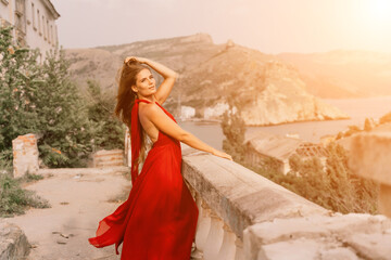Woman red dress. Summer lifestyle of a happy woman posing near a fence with balusters over the sea.