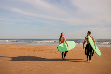 Young couple of surfers walking on the seashore with surfboards