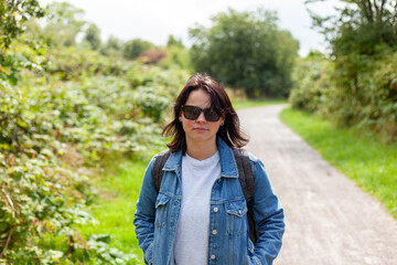 Portrait of a beautiful middle-aged woman in a denim jacket and sunglasses on a country road